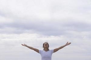 mujer en frente con camisa blanca levantando sus brazos hacia el cielo foto