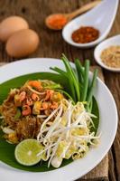 Pad thai con limón, huevos y condimentos sobre una mesa de madera foto