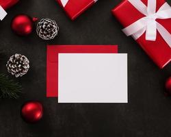 Tarjeta de felicitación blanca en blanco y maqueta de sobre con adornos de regalos de Navidad sobre fondo grunge foto