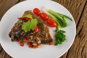 Deep-fried fish head topped with chilis on a white plate photo
