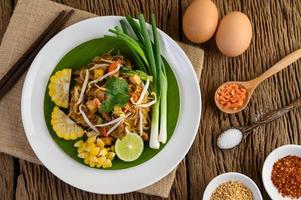 Pad thai con limón, huevos y condimentos sobre una mesa de madera foto