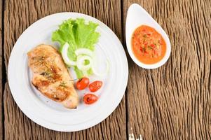 Grilled chicken on a wooden table with tomatoes, salad, onion and chili sauce photo