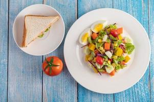 Fresh salad on a white plate with a sandwich and tomatoes photo