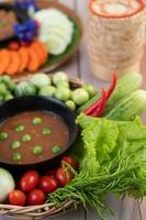 Chili paste paste in a bowl with eggplant, carrots, chili and cucumbers in a basket photo