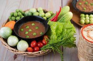 Chili paste paste in a bowl with eggplant, carrots, chili and cucumbers in a basket photo