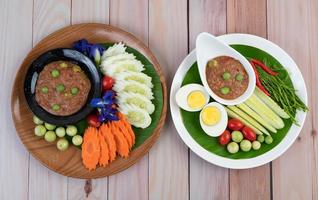 Chili paste paste in a bowl with eggplant, carrots, chili and cucumbers in a basket photo