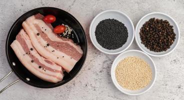 Pork belly in a pan with pepper seeds, tomatoes and spices photo