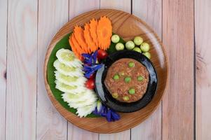 Chili paste paste in a bowl with eggplant, carrots, chili and cucumbers in a basket photo