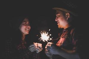 Feliz pareja sosteniendo fuegos artificiales de bengala en la noche foto