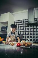 lindo niño aprendiendo a cocinar de pie en la cocina foto