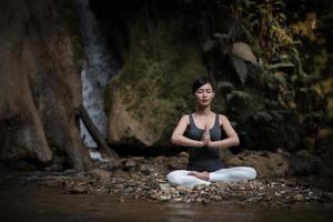 mujer joven en una pose de yoga sentado cerca de una cascada foto