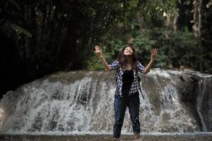 Young woman having fun under a waterfall in the forest photo