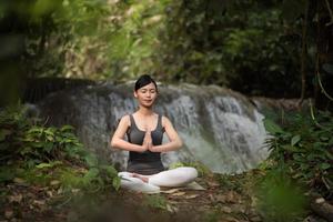 Young woman in a yoga pose sitting near a waterfall photo