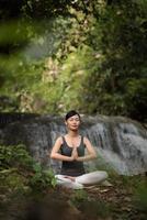 Young woman in a yoga pose sitting near a waterfall photo