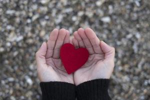 Corazón rojo entre las manos de una mujer sobre un fondo de piedras de playa concepto de San Valentín.