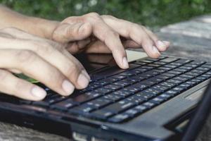 Persona de mano que trabaja y usa en una computadora portátil para autónomos con teclado de entrada para trabajo de blogger en línea en una computadora negra en una mesa de madera en casa. foto