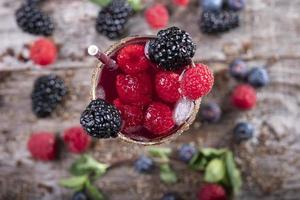 Cóctel de frutas del bosque en un vaso visto desde arriba sobre una base de madera decorada con moras foto