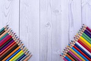 Lápices de madera de colores, en las esquinas inferiores de un fondo de madera gris y blanco foto