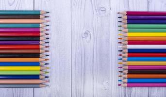 Lápices de madera de colores, uno frente al otro, sobre un fondo de madera gris y blanco foto