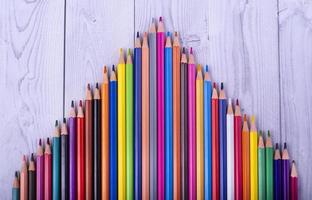Lápices de madera de colores, formando un triángulo, sobre un fondo de madera blanca y gris foto