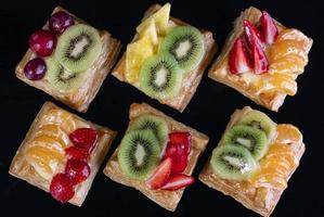 Puff pastry with tangerine, kiwi and strawberry fruit on black background viewed from above photo