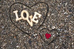 Letras de madera que forman la palabra amor con un corazón rojo sobre un fondo de arena de playa, dentro de un corazón hecho con los dedos. concepto de san valentin