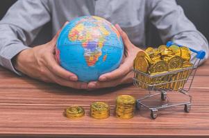 mano sosteniendo un globo terráqueo y monedas en el escritorio foto