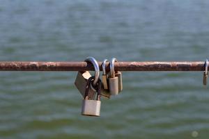 Multiple padlocks on a metal bar with a water background photo