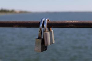 Two padlocks on a metal bar with water and the horizon in the background photo