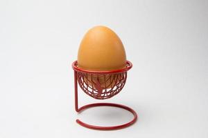 Un huevo de gallina en una canasta metálica roja sobre un fondo blanco. foto