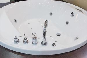 Bathtub faucet in modern bathroom. White bath tub with faucet and beige tiles. Detail of bathroom, selective focus photo