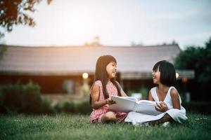 Two little girls in the park on the grass reading a book and learning photo