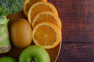 Orange slices with apple, kiwi and broccoli on a wooden plate photo