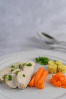 Steamed chicken breast on a white plate with spring onions, baby corn and carrots