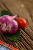 Cebollas rojas, tomates y hojas de lima kaffir sobre una mesa de madera foto