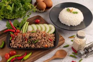 Spicy minced pork salad with rice, chili's, and tomatoes on a black plate photo