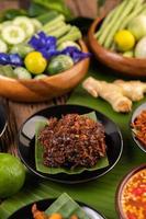 Chili paste served on banana leaves surrounded by long beans, lime, chili and eggplant photo