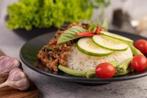 Ensalada picante de cerdo picada con arroz, chili y tomates en una placa negra foto