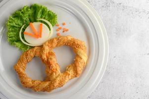 Pretzel on a white dish with lettuce and carrots photo