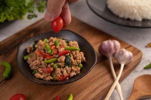 Spicy minced pork salad with rice, chili's, and tomatoes on a black plate photo