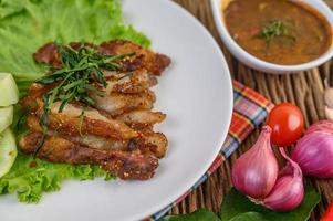 Pork neck grilled on a white plate with red onion, tomato and chili on a wooden table photo