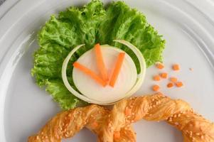 Pretzel on a white dish with lettuce and carrots photo