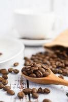 Coffee beans in a wooden spoon and hemp sacks on a white wood table photo