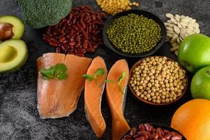 Legumes, broccoli, fruit, and salmon on a black cement background photo