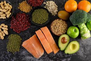 Legumes, broccoli, fruit, and salmon on a black cement background photo