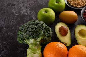 Broccoli, apple, orange, kiwi and avocado on a black cement floor background photo