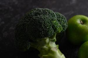 Broccoli, apple and avocado on a black cement floor background photo