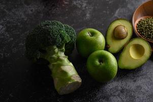 Broccoli, apple and avocado on a black cement floor background