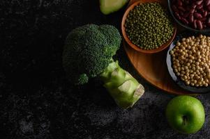 Broccoli, apple and beans on a black cement floor background photo