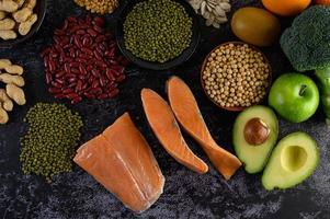 Legumes, broccoli, fruit, and salmon on a black cement background